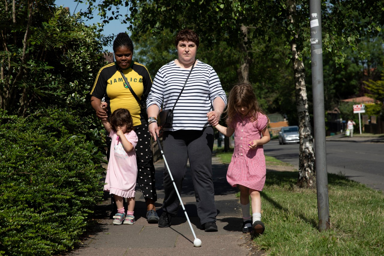 Charmaine uses her cane to guide her as she walks her two daughters home from school
