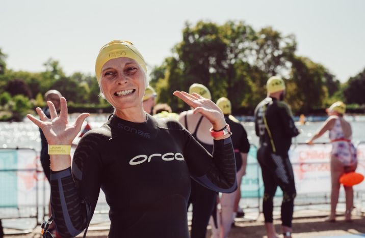 Image shows a lady smiling with her hands in the air after taking part in the Swim Serpentine
