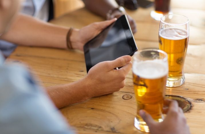 Image shows a gentleman taking part in a pub quiz on his iPad whilst drinking a pint of beer.
