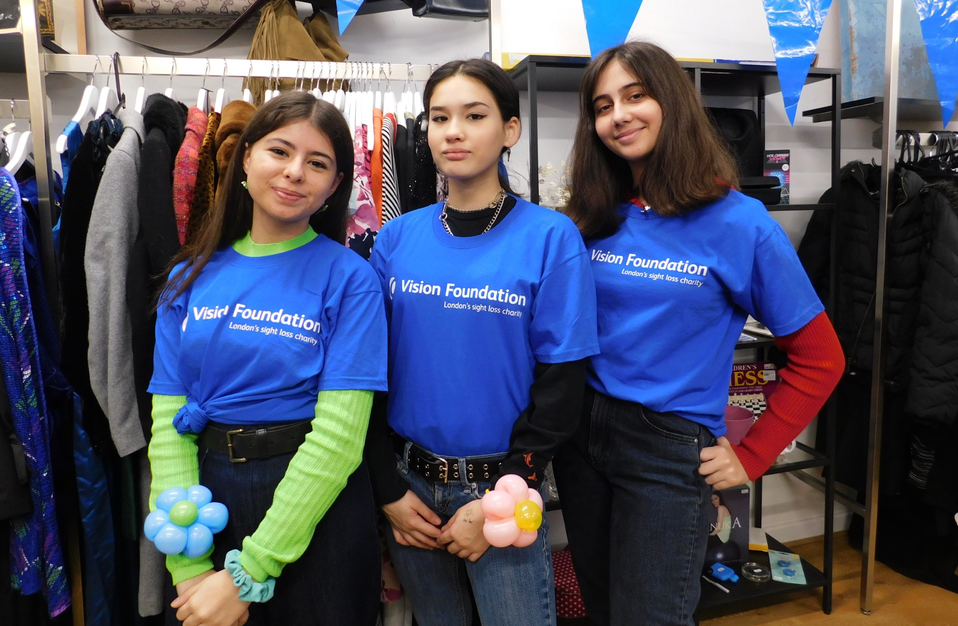 three shop volunteers pose wearing blue Vision Foundation t-shirts