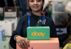 Brinda stands in the warehouse holding two coloured eBay boxes