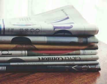 A stack of printed newspapers on a wooden table
