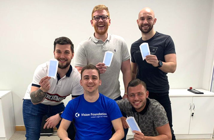Five men in their 20s, 4 holding wax strips as one of the team prepares to be waxed for charity