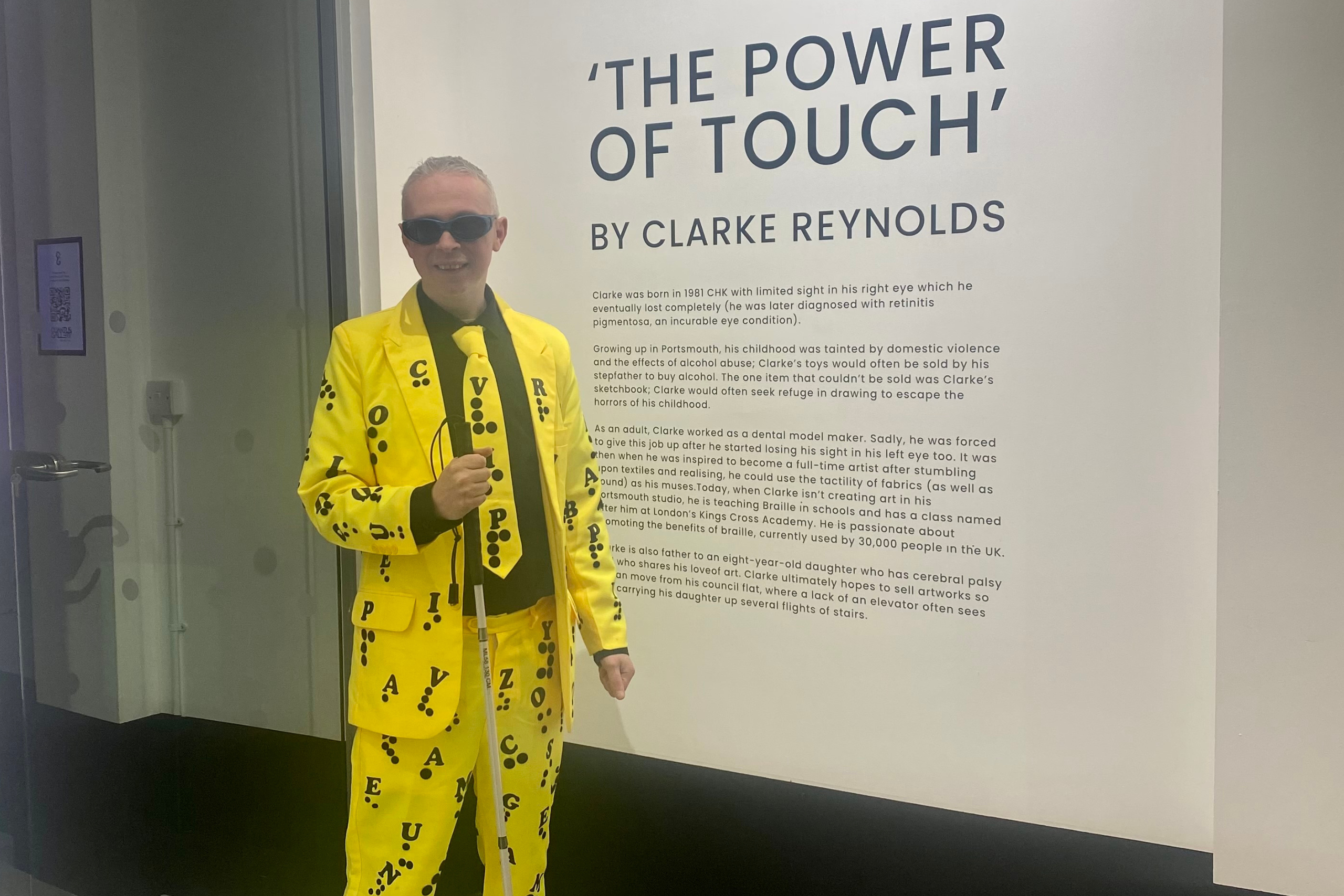 Clarke Reynolds wearing a yellow suit covered in Braille letters.