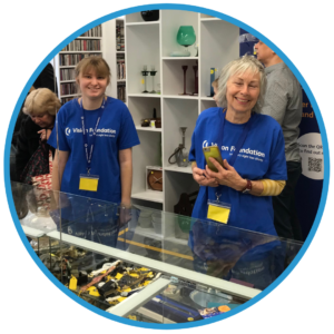 Two volunteers smiling by the charity shop jewellery counter (Super Big Helpers)
