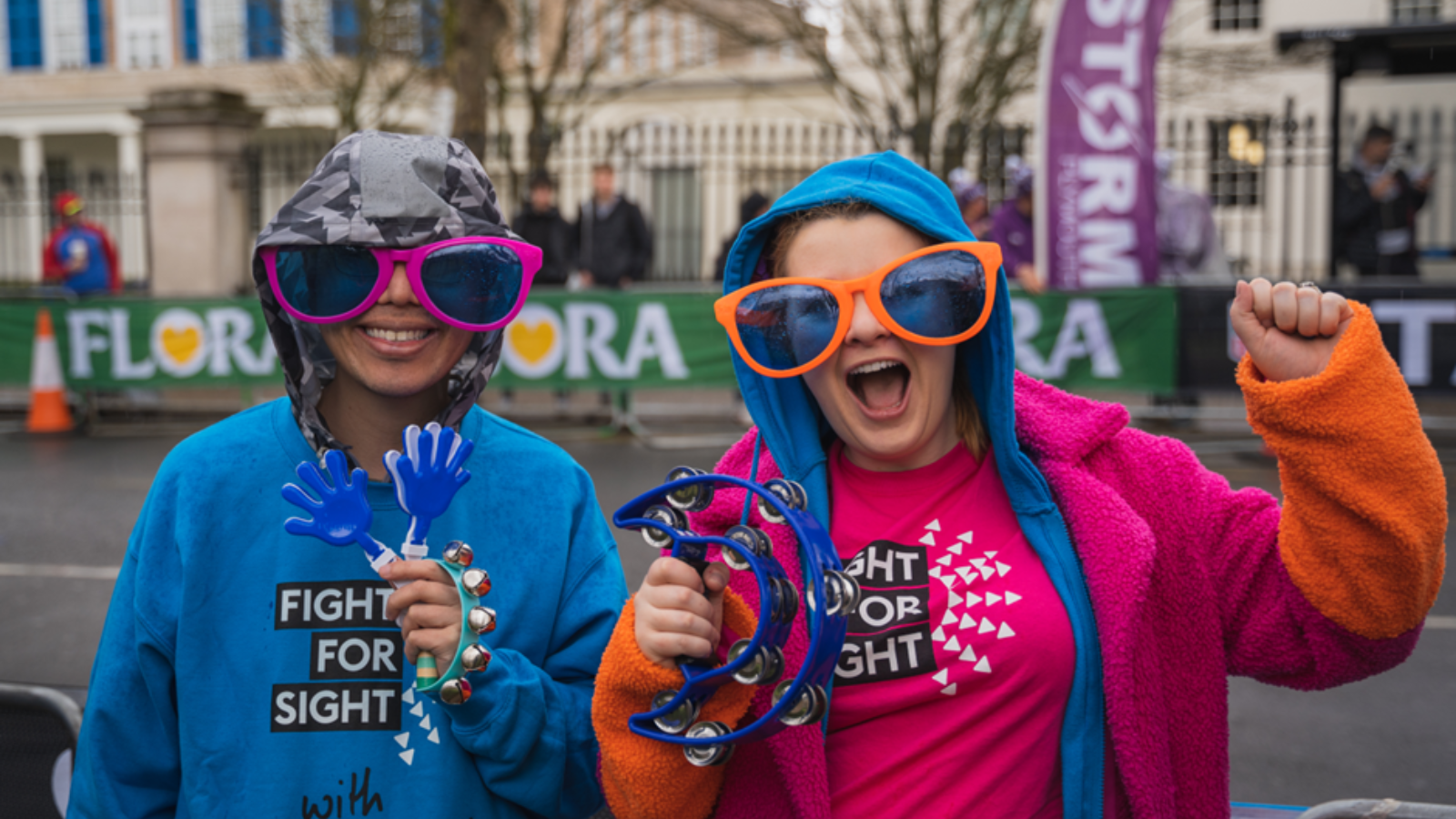 Two people in Fight for Sight jumpers wearing massive sunglasses and smiling.